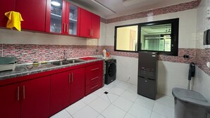 A kitchen with red cabinets, a sink, a washing machine, and a refrigerator. - EDS Hébergement meublé (Abidjan)