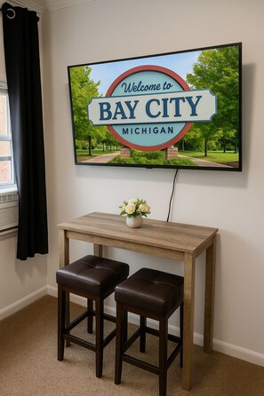 A framed welcome sign for Bay City, Michigan, mounted on a wall above a wooden table with two leather stools.