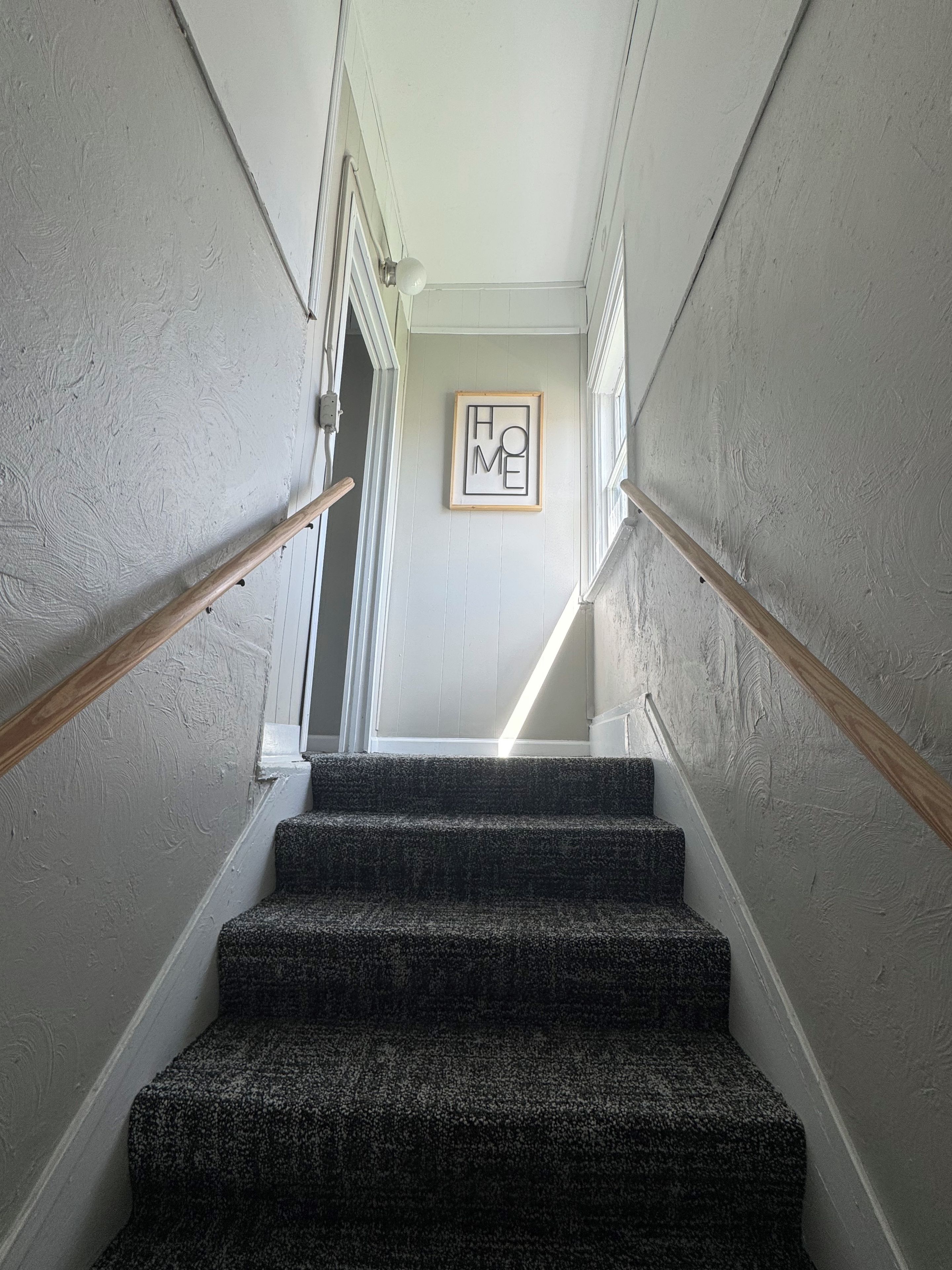A staircase with a handrail, carpeted steps, and a framed 'HOME' sign on the wall.