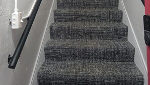 Una escalera con alfombra, barandales y un cuadro con la palabra 'HOME'.
