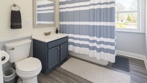 Un baño con inodoro, lavamanos, espejo y cortina de ducha a rayas.