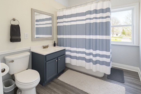 Une salle de bain équipée de toilettes, d’un lavabo, d’un miroir et d’un rideau de douche à rayures.