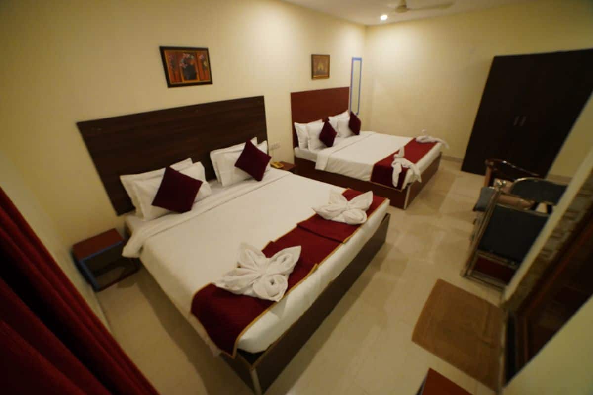 Habitación de hotel con dos camas, cada una con ropa blanca y detalles rojos, cabeceros de madera y cortinas rojas.