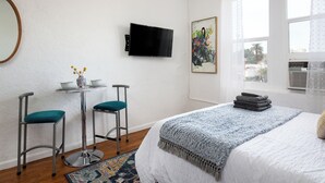 A bedroom with a bed, a TV mounted on the wall, a small table with two chairs, and a window with curtains. - Cozy studio in beautiful Los Angeles with air conditioning (Los Angeles)