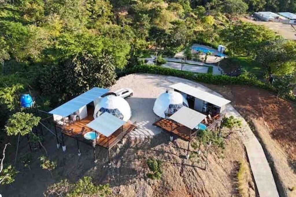 Un edificio de forma abovedada con techo plano, rodeado de árboles y cielo despejado.