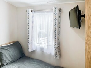 A bedroom with a bed, a TV mounted on the wall, and a window with a curtain. - 2 bedroom accommodation in Sandown (Sandown)