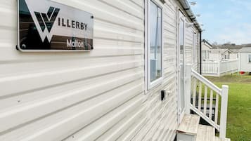 A mobile home with a sign that reads 'WILLERBY Malton' and a wooden staircase leading to a deck.