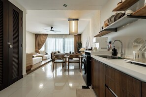A modern kitchen with a dishwasher, sink, and wooden cabinets. There is a dining area with a table and chairs. - 4Pax Studio 300m Walk to Setia City Mall (Shah Alam)