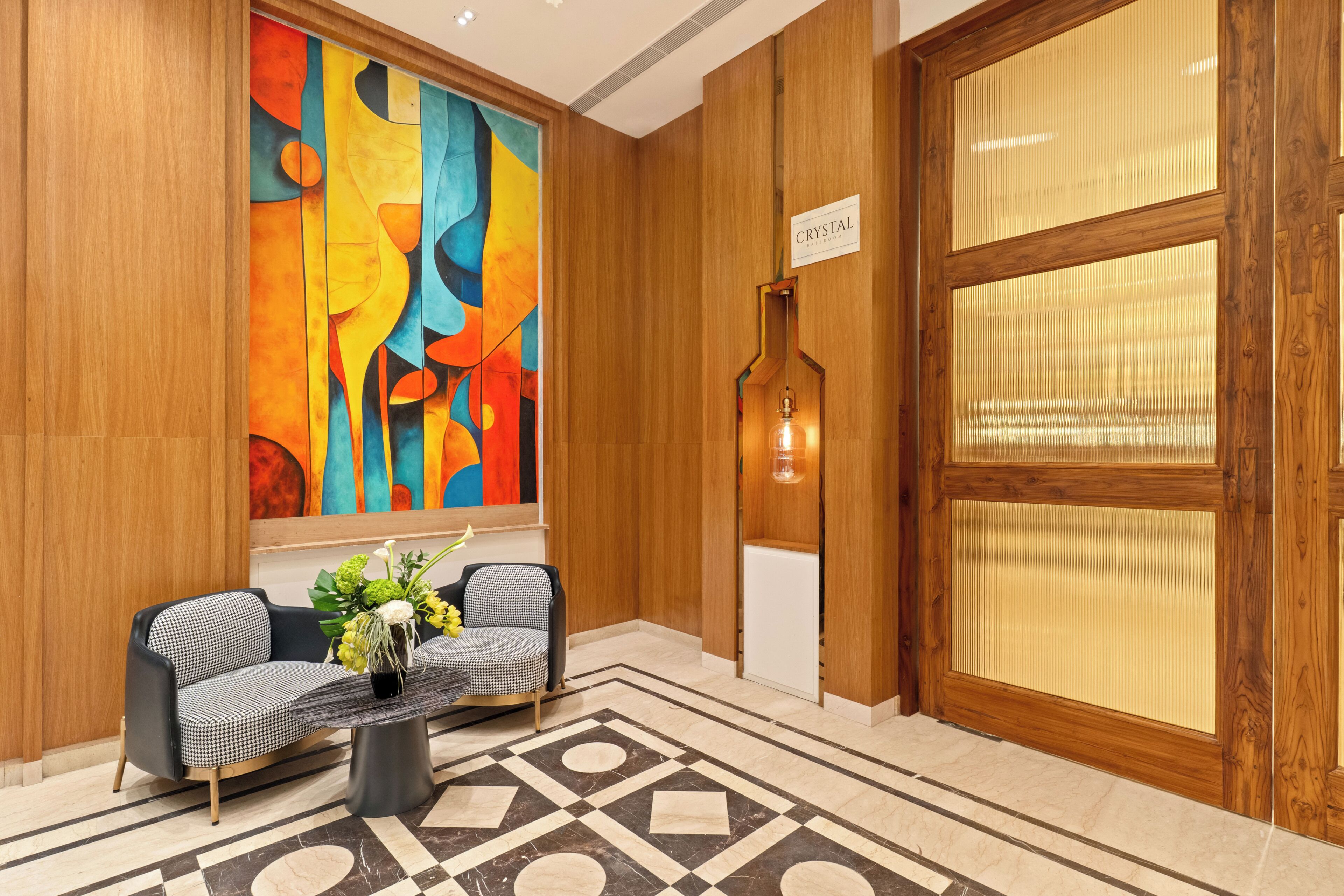 A lobby with a checkered sofa, a vase with flowers, a large abstract painting, and a wooden door labeled 'CRYSTAL.'