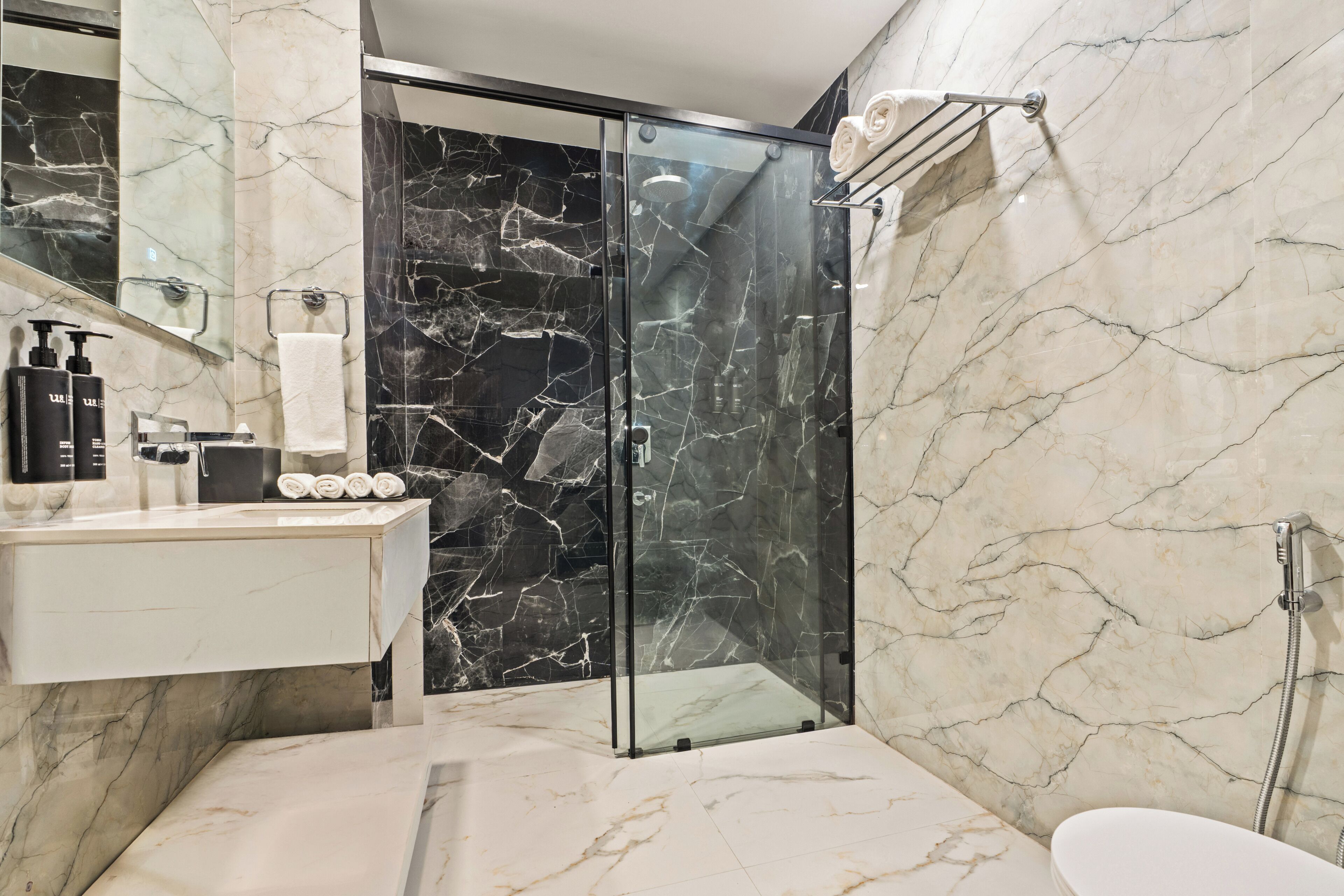 A modern bathroom with a glass-enclosed shower, a white sink with toiletries, and marble walls.