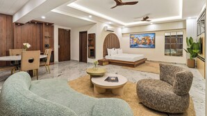 Habitació d'hotel moderna amb zona de menjador, sofà, taula de cafè, llit i ventilador de sostre.