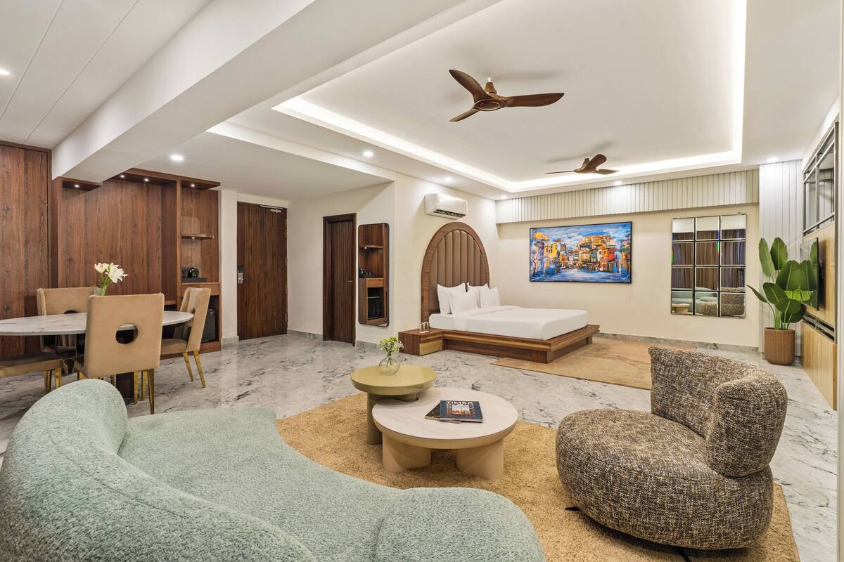 Habitación de hotel moderna con zona de comedor, sofá, mesa de centro, cama y ventilador de techo.