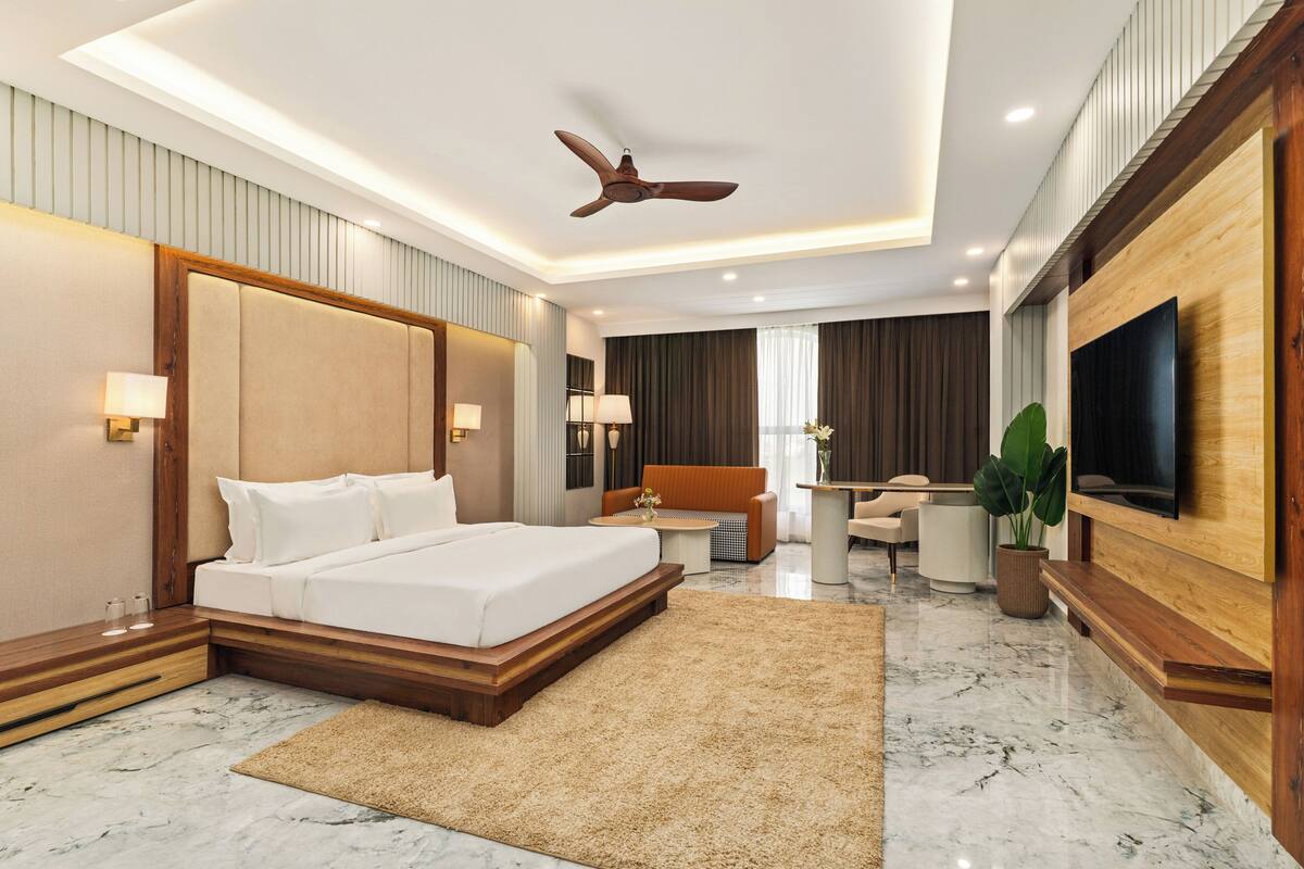 Una habitación de hotel moderna con una cama grande, un escritorio, una silla, un televisor y un ventilador de techo.