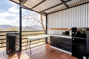 Ein Balkon mit Holzboden, Metallgeländer, einem Tisch und einer Grillstation in Schwarz.