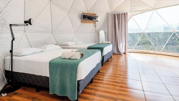 A room with a geometric ceiling, two beds with green blankets, a desk with a lamp, and a window with a view. - Glamping Dome Potrero Nº 4: Space, Nature and Comfort with Private Pool (Potrero)