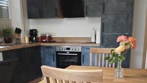 A wooden dining table with chairs, a kitchen with dark cabinets, and a vase with flowers on the table. - Apartment with mountain view, 60sqm & balcony (Waging am See)