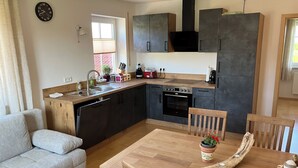 A modern kitchen with a dining area, wooden furniture, and a built-in oven. - Apartment with mountain view, 60sqm & balcony (Waging am See)