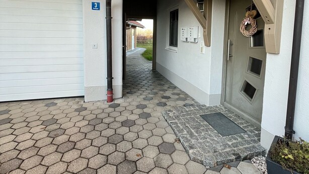 A building with a garage, a covered entrance, and a hexagonal tile driveway. - Apartment with mountain view, 60sqm & balcony (Waging am See)