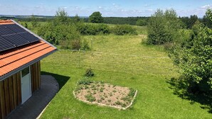 A building with a solar panel roof, a garden with a raised flower bed, and a fenced area with trees and shrubs. - Apartment with mountain view, 60sqm & balcony (Waging am See)