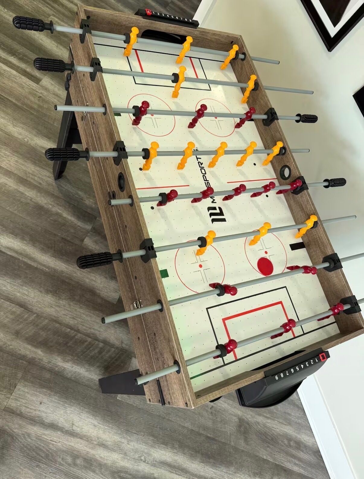 Une table de baby-foot avec un cadre en bois et une surface de jeu blanche.