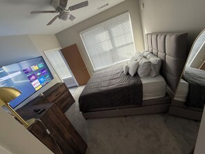 A bedroom with a bed, a TV, a ceiling fan, and a window with blinds. - Welcome to your fun 2BR/2BA arcade loft—relax, play, and enjoy your stay!! (Atlanta)