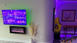 A living room with a flat-screen TV, a foosball table, a framed picture, and a vase with pampas grass. - Welcome to your fun 2BR/2BA arcade loft—relax, play, and enjoy your stay!! (Atlanta)