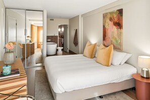 A modern hotel room with a large bed, a bedside table, a mirror, and a bathroom visible through an open door. - Apartment R111 - Designer Style and Elegance (Scarborough)
