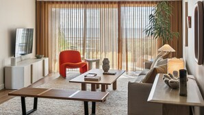 Un salon moderne avec un téléviseur à écran plat, un fauteuil rouge, une table basse en bois, un canapé et une grande fenêtre avec des rideaux.