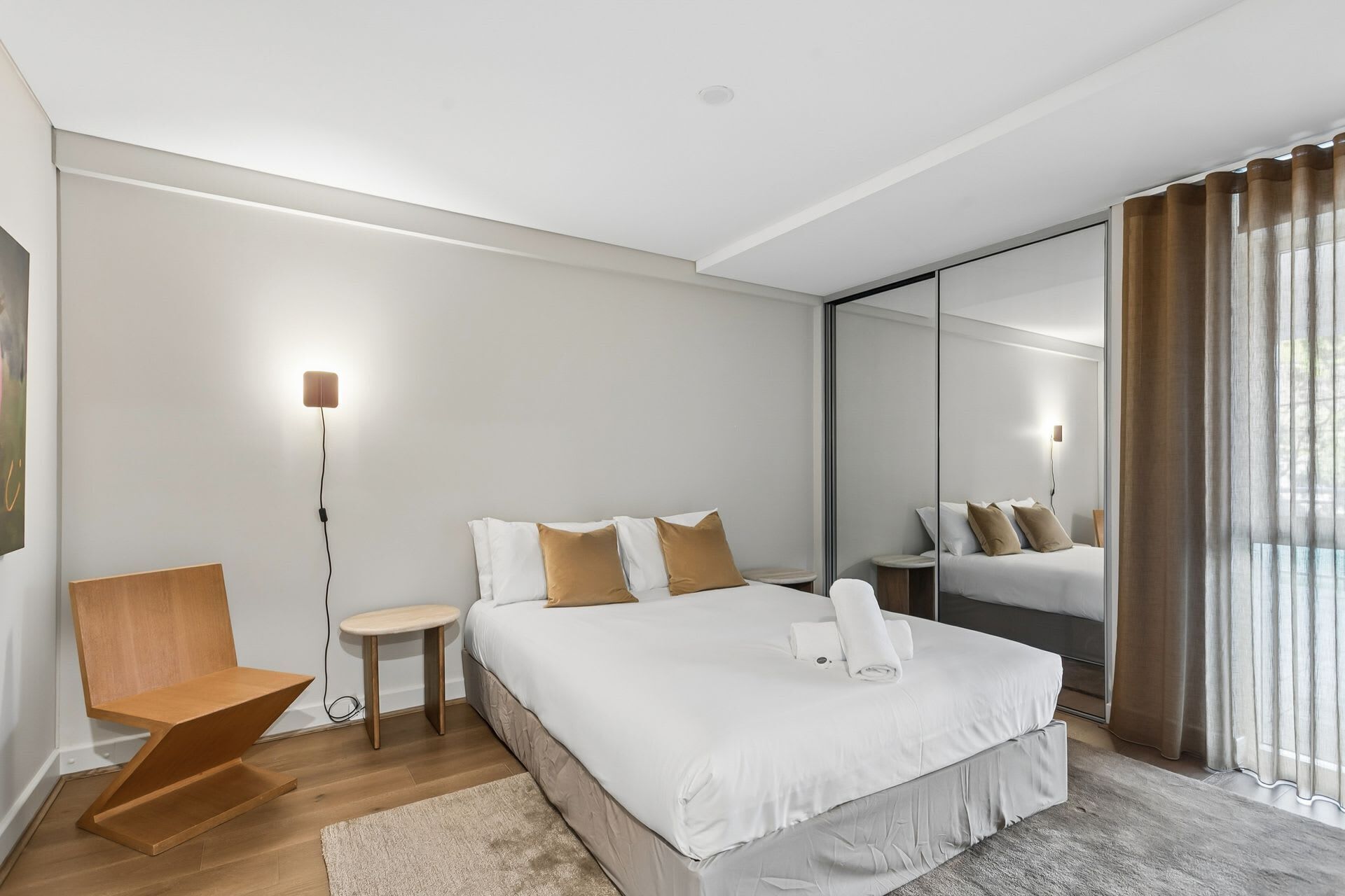 Ein modernes Hotelzimmer mit einem großen Bett, einem kleinen Nachttisch, einem Sessel, einer Nachttischlampe und einem großen Spiegel.
