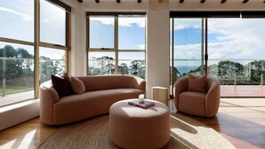 A spacious living room with large windows, a round ottoman, and a sofa. - The Hemp House | Table Cape Ocean Views (Table Cape)