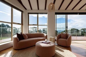 A spacious living room with large windows, a round ottoman, and a sofa.