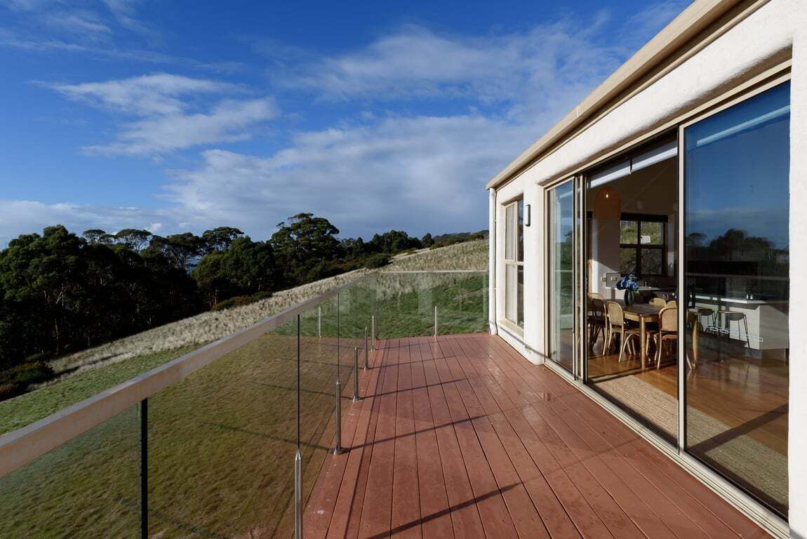 Une maison moderne dotée d’une terrasse en bois, de grandes portes-fenêtres coulissantes et offrant une vue sur le paysage environnant.