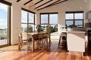 A modern kitchen with large windows, a dining area with wooden furniture, and a view of the outdoors.