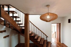 A wooden staircase with a metal railing, a hanging light fixture, and a door leading to another room. - The Hemp House | Table Cape Ocean Views (Table Cape)
