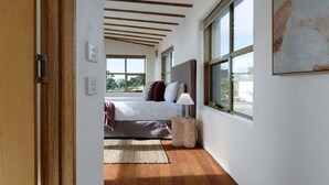 A bedroom with a bed, a bedside lamp, a rug, and large windows. - The Hemp House | Table Cape Ocean Views (Table Cape)
