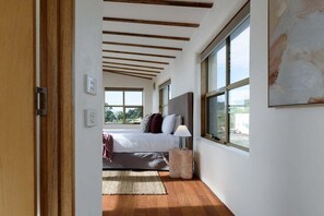 A bedroom with a bed, a bedside lamp, a rug, and large windows. - The Hemp House | Table Cape Ocean Views (Table Cape)