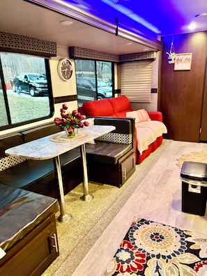 Een compact RV-interieur met een bed, zithoek, tafel en uitzicht door het raam.