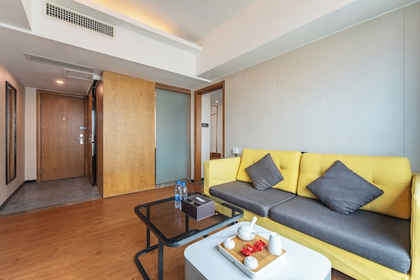 Una habitación de hotel moderna con un sofá amarillo, una mesita de centro de vidrio y una puerta de madera.