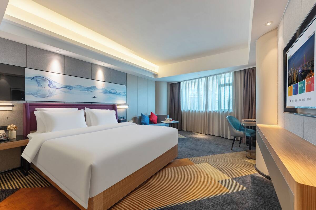 Ein modernes Hotelzimmer mit einem großen Bett, einem Schreibtisch, einem Stuhl und einem Fernseher.
