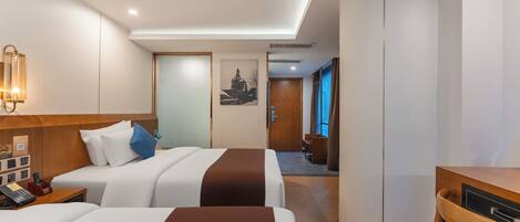 A hotel room with two beds, a desk, a chair, a phone, a lamp, and a picture on the wall.