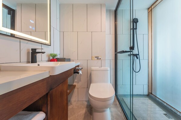 A modern bathroom with a white toilet, a wooden vanity, a large mirror, and a glass-enclosed shower area.