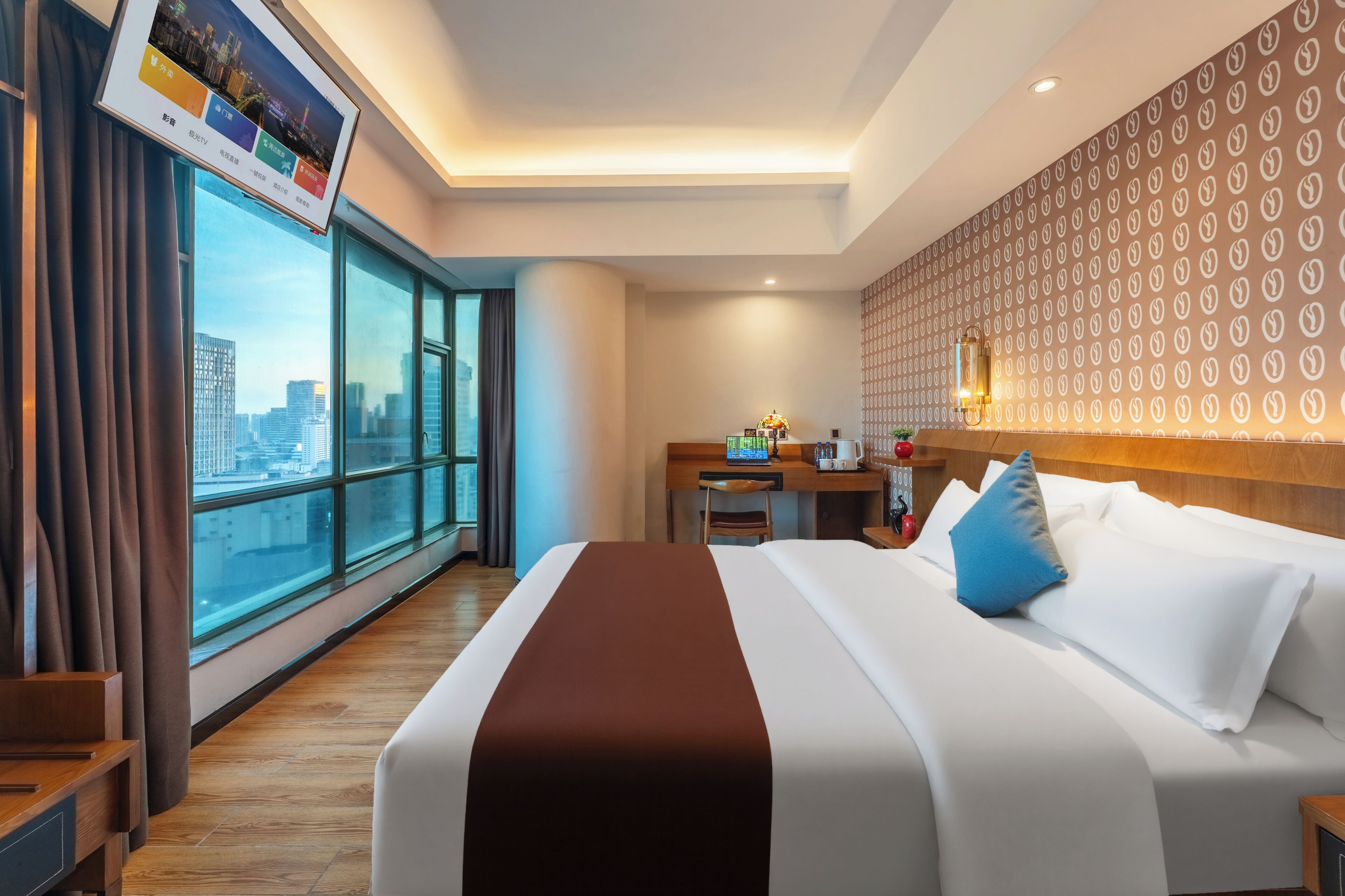 Una habitación de hotel con un ventanal grande, una cama con ropa de cama blanca y marrón, un escritorio con una computadora portátil y vistas a la ciudad.