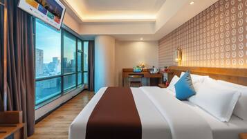 Una habitación de hotel con un ventanal grande, una cama con ropa de cama blanca y marrón, un escritorio con una computadora portátil y vistas a la ciudad.