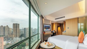 Habitación de hotel con un ventanal grande, una cama, una mesita con bandeja y un escritorio con computadora.