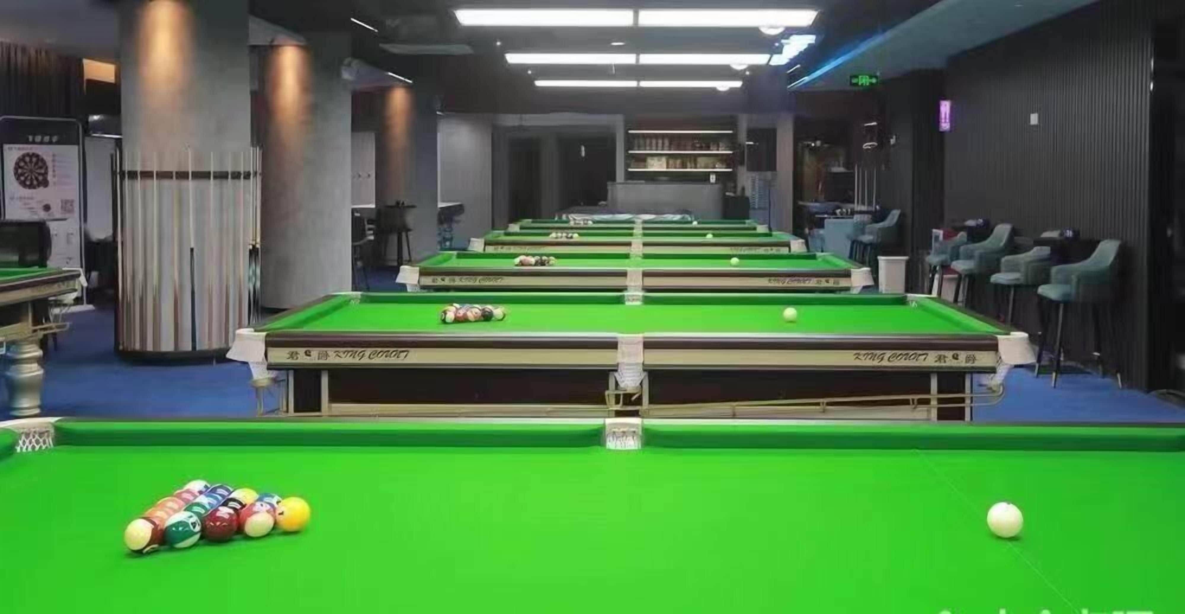 A pool hall with multiple tables, chairs, and a green pool table in the foreground.