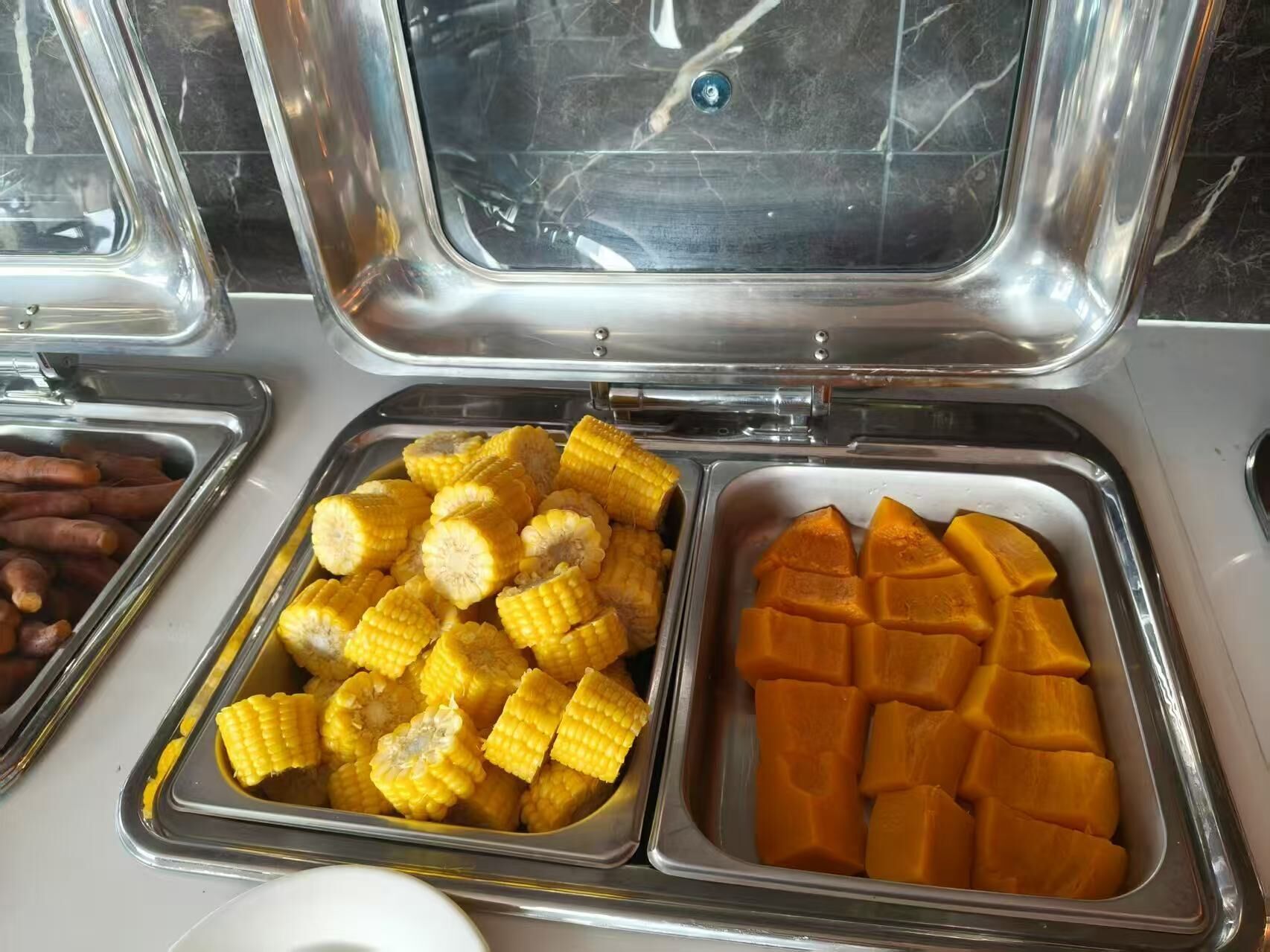 Un bufé con diversos alimentos, incluyendo trozos de maíz y mango.