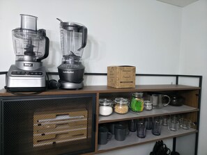 A kitchen with two blenders, a box labeled 'Elite Gourmet,' and various kitchenware on shelves.