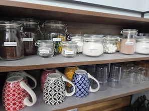 A shelf with various glass jars labeled with different food items like instant coffee, orange pekoe, and black tea.