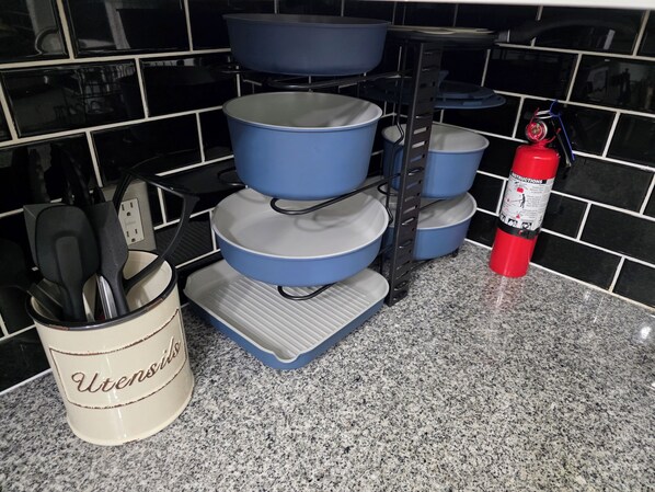 A kitchen with a black tiled backsplash, a blue pot rack, a white utensil holder, and a red fire extinguisher.