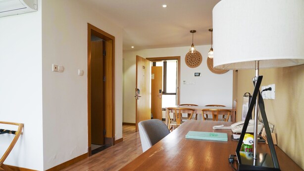 Une pièce comprenant une table à manger en bois, des chaises, une lampe et une porte donnant sur une autre pièce.
